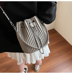 Detail of light gray pleated bucket bag with silver chain strap and leather handle