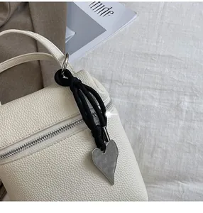 Détail du sac bandoulière en cuir litchi blanc cassé avec breloque cœur argentée et sangle