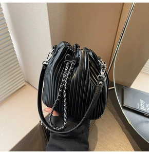 Close-up of black pleated bucket bag with chain strap and leather handle drawstring design