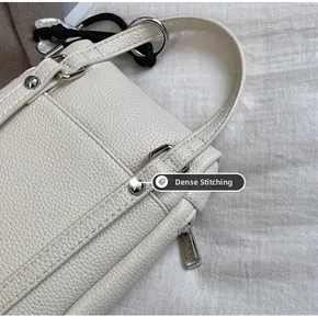 Gros plan du cuir grainé avec clous argentés et coutures fines sur un sac beige chic