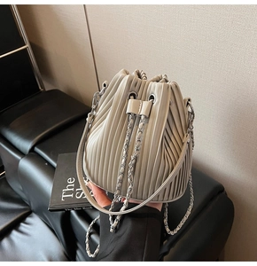 Detail of light beige pleated bucket bag with drawstring closure and silver chain strap