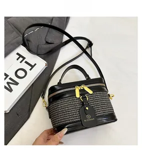 Detail view of woven leather box bag with gold zippers and brand tag on grey blazer