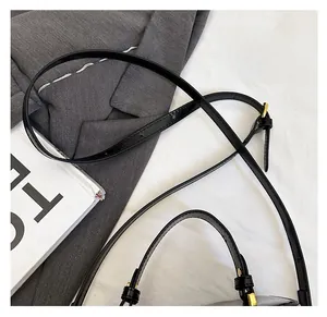 Close-up of black glossy leather bag showing the adjustable shoulder strap and gold buckle