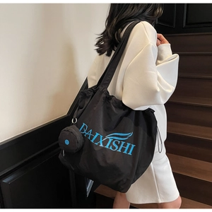 Detail shot of black tote bag with blue lettering and matching small round pouch on shoulder