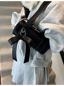 Sac cylindrique noir chic avec grand nœud porté par un mannequin sur des escaliers