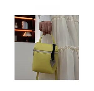 Detail of yellow lychee pattern cross-body bag featuring metal heart charm and handle
