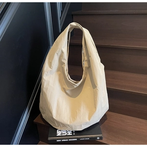 Dettaglio della trama di una borsa tote beige in nylon su un gradino di legno con luce laterale