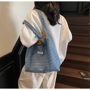 Detail of blue textured tote bag featuring a white LOVE patch and brown lining