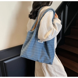 Detail shot of a blue striped knit tote bag with a small Love label worn on shoulder