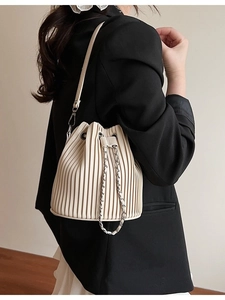 Beige pleated bucket bag with chain drawstring and leather strap on a model's shoulder