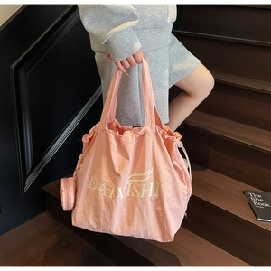 Pink drawstring tote bag featuring golden logo and matching circular pouch on stairs