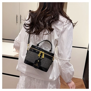 Detail of a black bucket bag showing glossy patent leather and woven texture with gold zippers