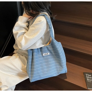 Detail of blue striped canvas tote bag with LOVE patch on brown wooden stairs