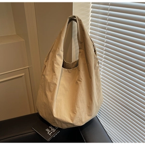 Dettaglio della borsa tote beige a pieghe con tracolla larga su divano in pelle