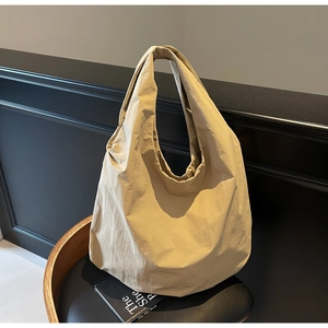 Dettaglio di una borsa hobo beige minimalista con ampia tracolla appoggiata su una sedia