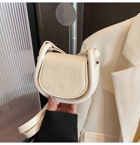 Macro shot of cream PU saddle bag with embossed bear pattern and sturdy ring handle