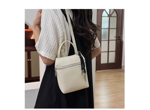 Model wearing cream litchi texture mini crossbody bag with heart charm detail