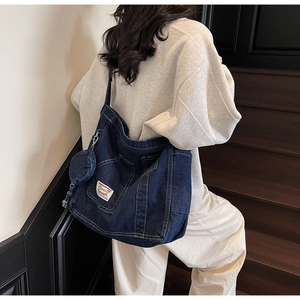 Detail of dark blue denim tote bag featuring external pocket and round coin purse attachment