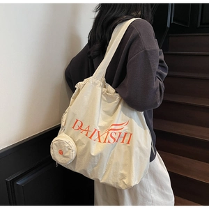 Detail of cream canvas tote bag with orange artistic lettering and mini side pouch accessory