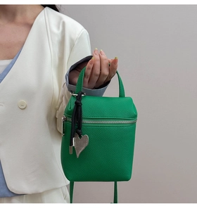Détail du sac bandoulière vert en cuir litchi avec pendentif coeur et fermeture éclair