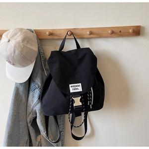 Detail of black nylon backpack featuring a brand label and silver buckle on a hanger