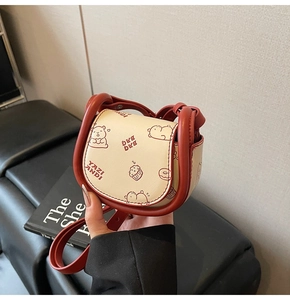 Close-up of cream mini saddle bag featuring cute cartoon bear and cupcake illustrations