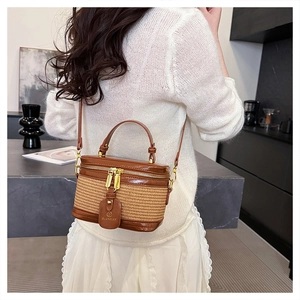 Detail view of cylindrical straw and leather crossbody box bag shown on female model