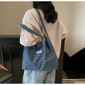 Detailed texture of a blue striped canvas tote bag with a LOVE patch on a model