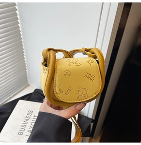 Detailed view of yellow mini saddle bag with embossed bear patterns and top handle
