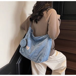 Detail of light blue washed denim tote bag with functional pockets and mini coin purse charm