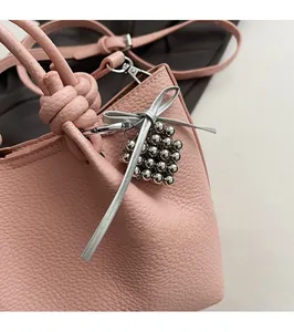 Detail of pink lychee leather handbag featuring grape bead charm and knotted handle