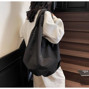 Grande borsa tote nera in nylon indossata a spalla da una modella su una scala