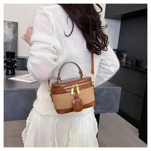 Detail view of woven straw box bag with brown leather trim and gold zippers