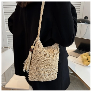 Detailed close-up of straw woven crossbody bag with hollow flower pattern and tassel charm