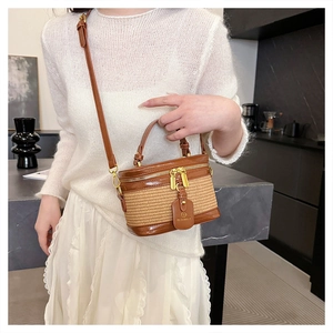 Detail of cylindrical straw handbag with brown leather trim and golden zippers