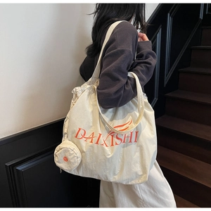 Detail of a beige drawstring canvas tote bag with side pocket and orange letter print
