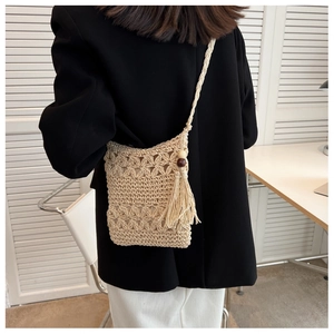 Detail of hollow woven straw phone bag with tassel charm and wooden bead accents