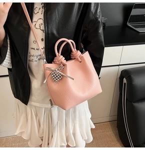 Detail of pink lychee textured bucket bag featuring heart charm and silver bow accent
