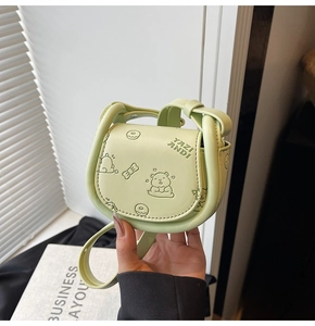 Close-up of light green crossbody saddle bag with embossed bear and donut patterns