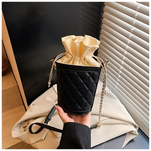 Close-up of black quilted bucket bag with cream drawstring and gold chain strap