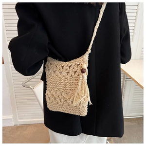 Detail of straw crossbody bag showing crochet floral texture, tassels, and wood beads