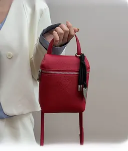Detail of red litchi texture mini bag with heart charm and tassel on white blazer