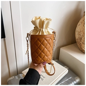 Close-up of quilted brown leather bucket bag with canvas drawstring and gold chain strap