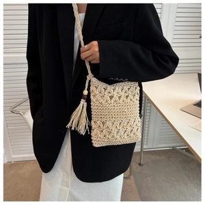 Detail of hollow straw phone bag with boho tassels and wooden beads on a woven shoulder strap