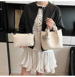 Detail of cream lychee leather bucket bag with knotted handle and metal ball charm