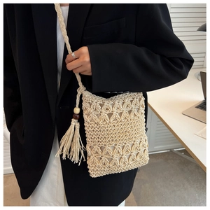Détail du sac en paille tissée avec découpes florales, pompons et perles en bois