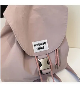 Detail of light purple nylon backpack showing silver buckle and logo tag on flap