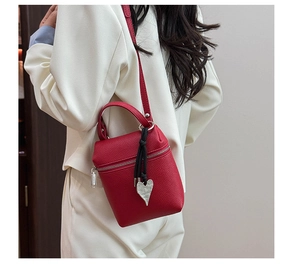 Détail du mini sac bandoulière rouge en cuir litchi avec pendentif cœur et fermeture éclair