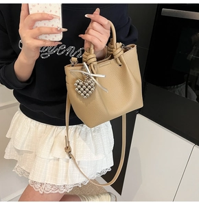Close-up of beige lychee texture bucket bag with knotted handle and heart charm detail