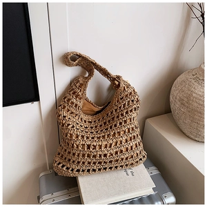 Close-up of brown hollow-out woven straw tote bag resting on a silver suitcase